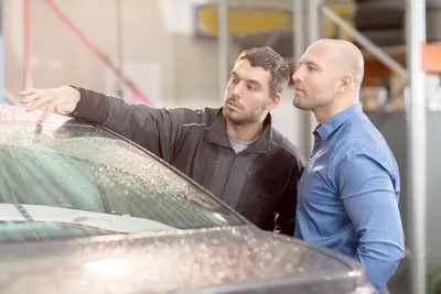 zwei männer stehen an einem nassen auto und inspizieren es