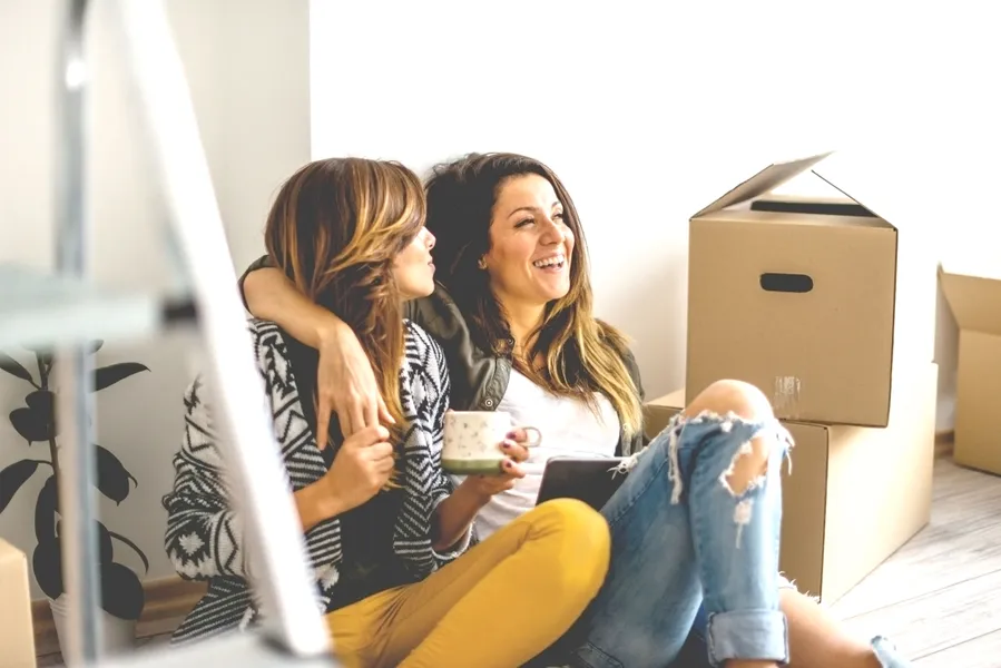 zwei frauen sitzen auf dem boden neben kartons und lachen