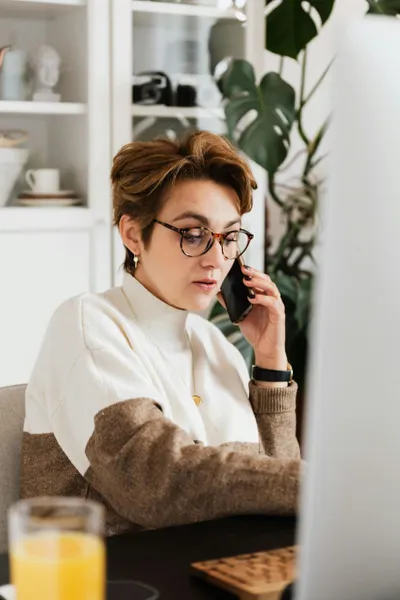 frau am schreibtisch mit handy am ohr