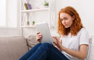 frau sitzt auf der couch und schaut auf das tablet