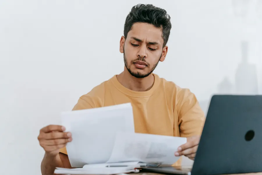 mann vor dem laptop mit dokumenten in der hand