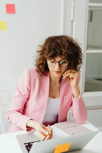 frau sitzt am tisch mit laptop und stift in der hand