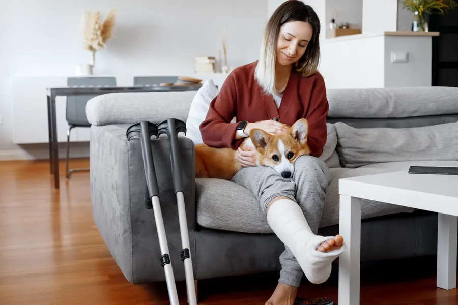 frau sitzt mit gebrochenen bein auf der couch und hat einen hund auf dem schoss