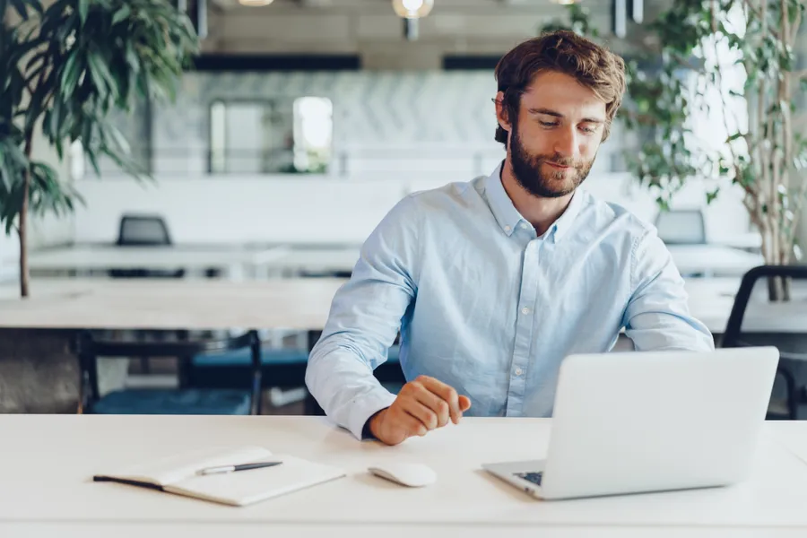 mann sitzt am schreibtisch und schaut auf sein laptop