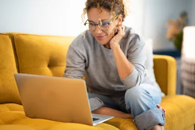 frau sitzt auf dem sofa und schaut auf laptop