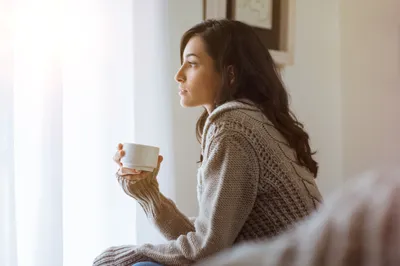 frau sitzt am fenster mit einer tasse in der hand