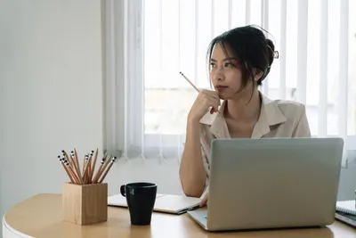 frau am schreibtisch mit laptop und stift in der hand