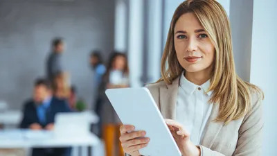 frau steht im büro mit tablet in der hand und lächelt in die kamera