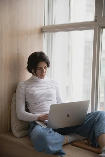 frau sitzt am fenster und recherchiert im internet