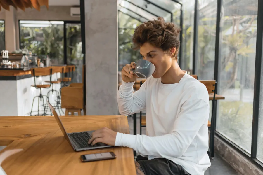 mann sitzt am laptop und trinkt einen kaffee